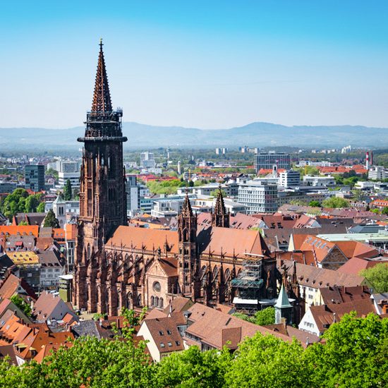 Münster von Freiburg im Breisgau mit markantem Turm, umgeben von modernen Gebäuden und grünen Landschaften.